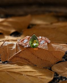 a green ring sitting on top of a leaf covered ground with leaves around it and two diamonds in the middle