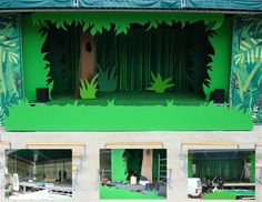 an outdoor stage with green curtains and plants on the wall, in front of a building