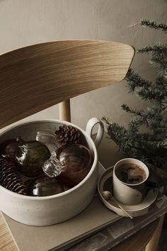 a white bowl filled with water next to a cup of coffee and a pine cone