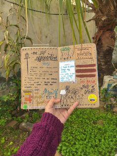 a person holding up a piece of cardboard with writing on it in front of a tree