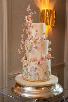 a three tiered wedding cake with pink flowers on the top and gold trimmings