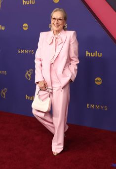 an older woman in a pink suit and matching heels poses for the camera on the red carpet