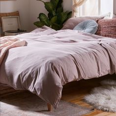 a bed with pink sheets and pillows in a bedroom next to a plant on the floor