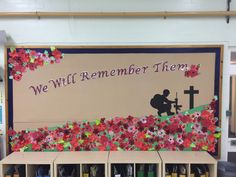 a bulletin board with paper flowers and a person kneeling at the cross in front of it that says, we will remember them