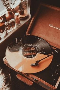 an old record player sitting on top of a wooden case next to a window with flowers