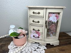 a white cabinet with flowers and beads on the floor next to it is a pink flower pot