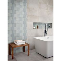 a white bath tub sitting next to a wooden bench in a bathroom with gray tiles on the walls