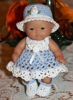 a small doll is wearing a crocheted dress and hat with flowers in the background