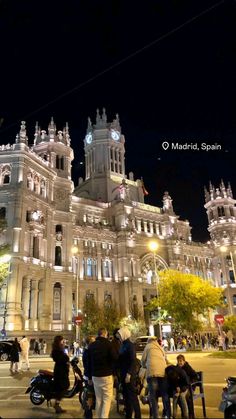 people are standing in front of a large building at night with lights on the top