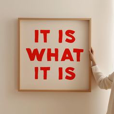 a woman is holding up a framed poster with the words it is what it is