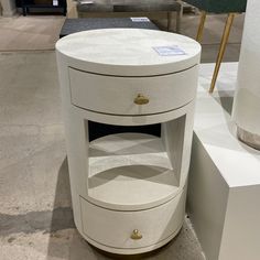 a white round table with two drawers on display in a room filled with other furniture