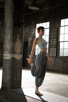 a woman standing on one leg with her legs crossed in the air, wearing grey pants and a crop top