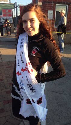 a woman is standing on the sidewalk with her scarf around her neck and smiling at the camera