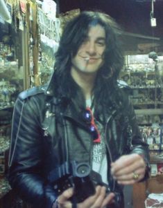 a man with long hair standing in front of a store filled with glassware and other items