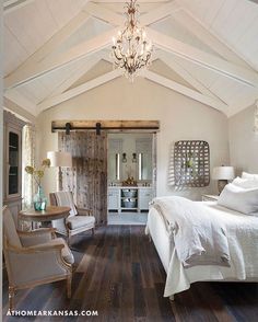 a white bedroom with wood floors and a chandelier hanging from the vaulted ceiling