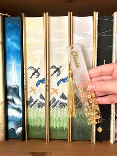 a hand is reaching for a book in front of some books on a wooden shelf