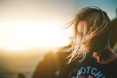 a person with long hair standing in front of the ocean at sunset or sunrise time