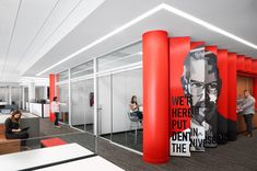 an office with red columns and posters on the walls, people working at their desks