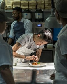 a man is preparing food in a kitchen while others watch him from behind the counter