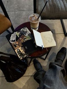 a person sitting at a small table with a book and drink on top of it