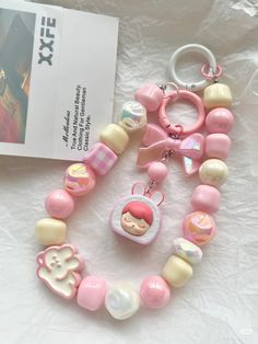 a pink and white necklace with charms on it next to a book, keychain and magazine