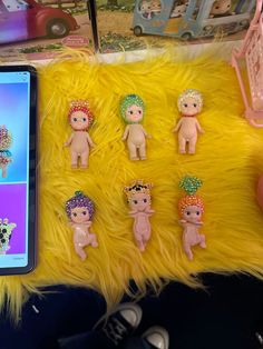 a cell phone is sitting next to some tiny dolls on a furry surface with other toys in the background