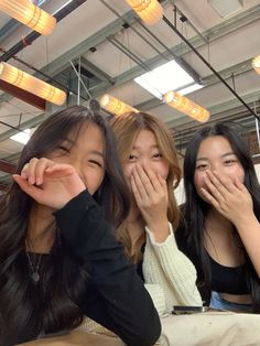 three young women sitting next to each other covering their mouths