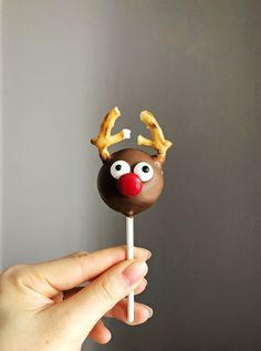 a hand holding a chocolate reindeer lollipop with eyes and nose on it's stick