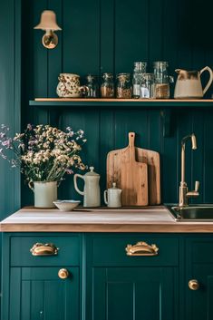 a kitchen with green painted cabinets and brass pulls on the cupboards is filled with flowers