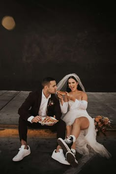 a bride and groom sitting on the ground eating pizza