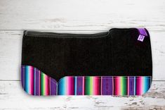 a black purse with multicolored stripes on the front and bottom, sitting on a white wooden surface