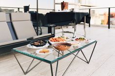 a glass table topped with plates of food on top of a hard wood floored patio