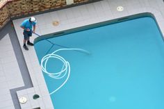 a man in blue shirt and white hat with a mop on top of a swimming pool