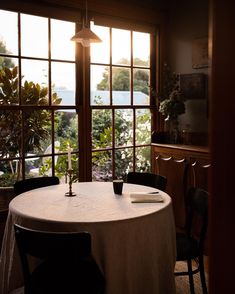 a table with a white cloth on it in front of two windows and some plants