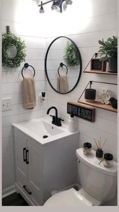 a white toilet sitting next to a bathroom sink under a round mirror on a wall