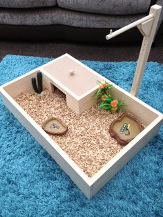 a miniature house made out of wood and sand in a living room area with blue rugs