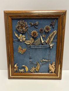 an old pair of jeans is decorated with flowers, leaves and other decorative items in a wooden frame