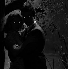 a man and woman standing next to each other in front of a tree with glowing eyes