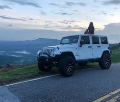 a white jeep parked on the side of a road with a woman standing on top