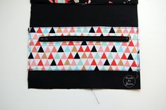 two zippered pouches are sitting on top of each other, one is black and the other is multicolored triangles