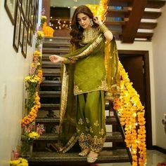 a woman in a green outfit standing on stairs with yellow flowers around her and holding onto the