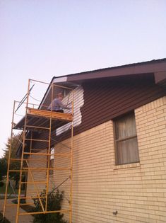 a man standing on a scaffold in front of a house with a ladder