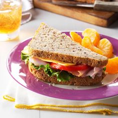 a purple plate topped with a sandwich and orange slices