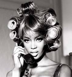 a black and white photo of a woman with curls on her head talking on the phone