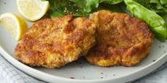 two chicken patties on a plate with greens and lemon wedges next to it