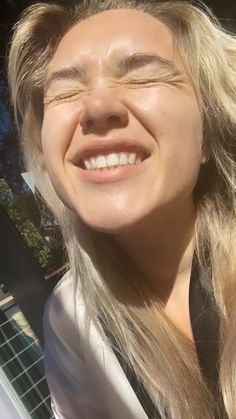 a close up of a person with long blonde hair and a white shirt smiling at the camera