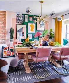 a dining room table with pink chairs and art on the wall in front of it