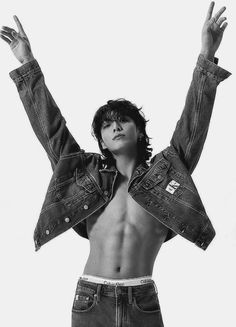 a shirtless man with his arms up in the air, wearing jeans and a jean jacket