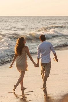 a man and woman walking on the beach holding hands