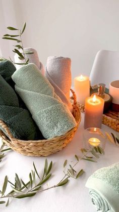 a basket filled with towels and candles on top of a white table covered in greenery